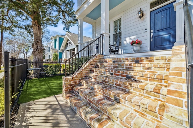 doorway to property featuring covered porch, a residential view, fence, and a yard