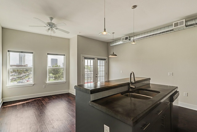 kitchen with a center island with sink, visible vents, dark countertops, decorative light fixtures, and a sink