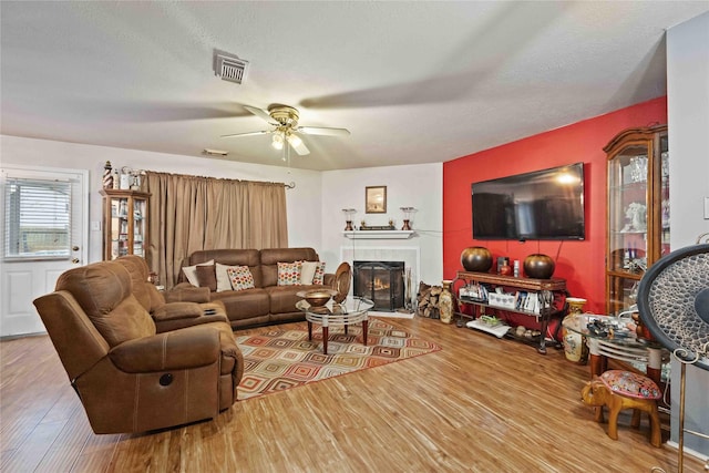 living room with visible vents, ceiling fan, wood finished floors, a textured ceiling, and a fireplace