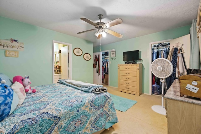 bedroom with a textured ceiling, ensuite bath, light carpet, and a walk in closet