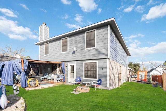 back of house with an outdoor fire pit, a lawn, a chimney, and fence