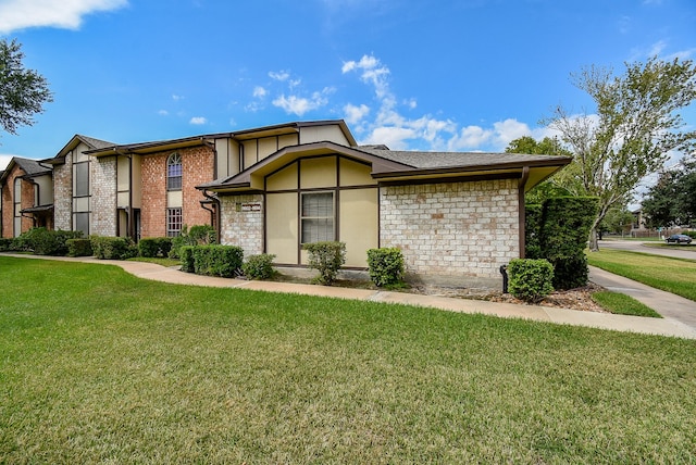 view of front of house featuring brick siding, a front lawn, and stucco siding