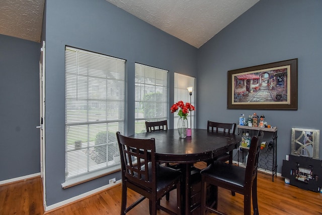 dining area with vaulted ceiling, a textured ceiling, wood finished floors, and baseboards