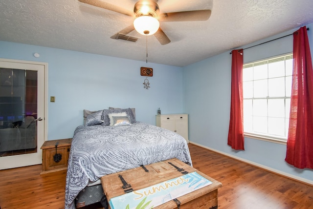 bedroom featuring visible vents, a ceiling fan, a textured ceiling, wood finished floors, and baseboards