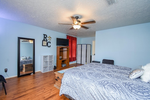 bedroom with visible vents, ceiling fan, a textured ceiling, wood finished floors, and baseboards