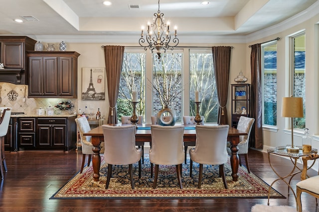 dining space with ornamental molding, a raised ceiling, dark wood finished floors, and a notable chandelier