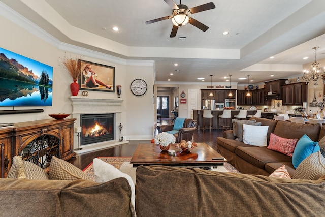 living area featuring a tray ceiling, dark wood-style flooring, a glass covered fireplace, and crown molding