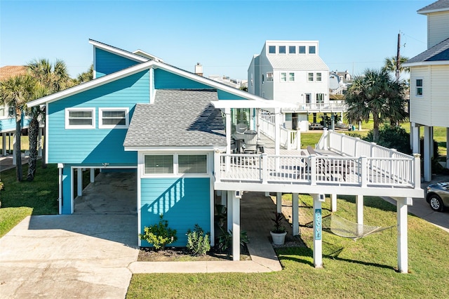 rear view of property with a carport, concrete driveway, roof with shingles, and a wooden deck