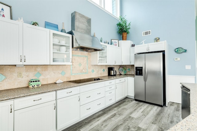 kitchen featuring black electric cooktop, visible vents, stainless steel refrigerator with ice dispenser, wall chimney exhaust hood, and glass insert cabinets