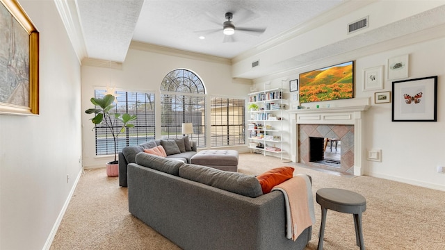 carpeted living room featuring a textured ceiling, visible vents, baseboards, a tiled fireplace, and crown molding