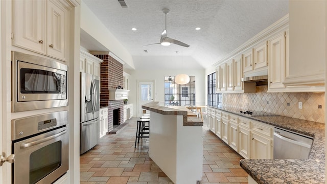 kitchen featuring lofted ceiling, appliances with stainless steel finishes, cream cabinets, under cabinet range hood, and a kitchen bar