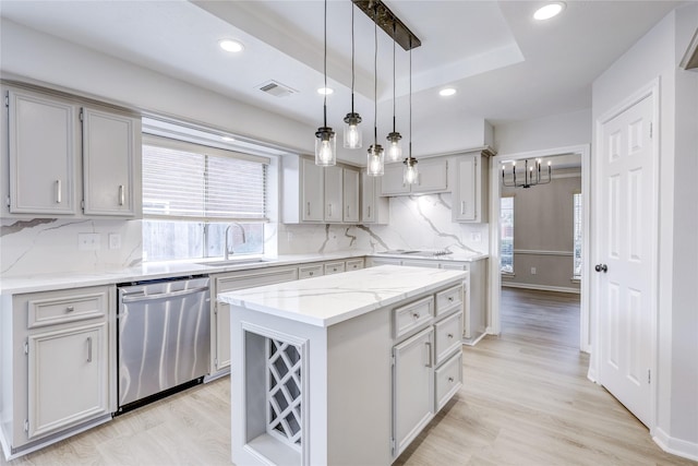 kitchen featuring a raised ceiling, a kitchen island, stainless steel dishwasher, pendant lighting, and a sink