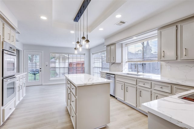 kitchen with visible vents, a kitchen island, hanging light fixtures, stainless steel appliances, and a sink