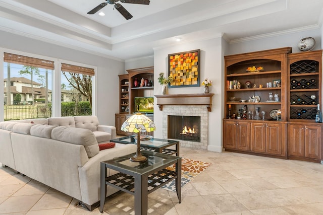 living area featuring a tray ceiling, crown molding, a lit fireplace, and ceiling fan