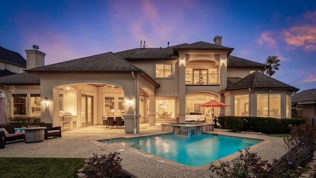 back of house at dusk with a balcony, a chimney, area for grilling, and a patio