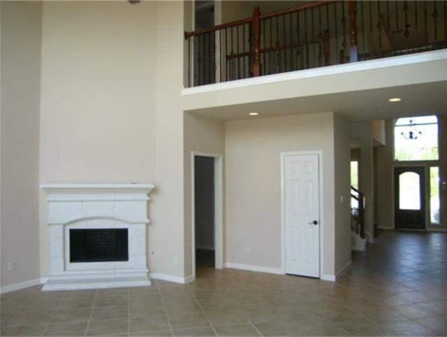 unfurnished living room featuring recessed lighting, a fireplace, a towering ceiling, and baseboards