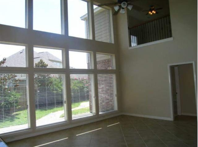 interior space with a ceiling fan, dark tile patterned flooring, a towering ceiling, and baseboards