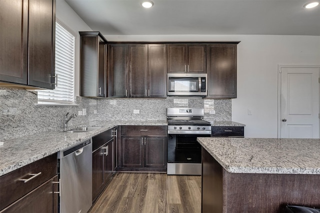 kitchen with dark wood finished floors, appliances with stainless steel finishes, light stone countertops, dark brown cabinets, and a sink