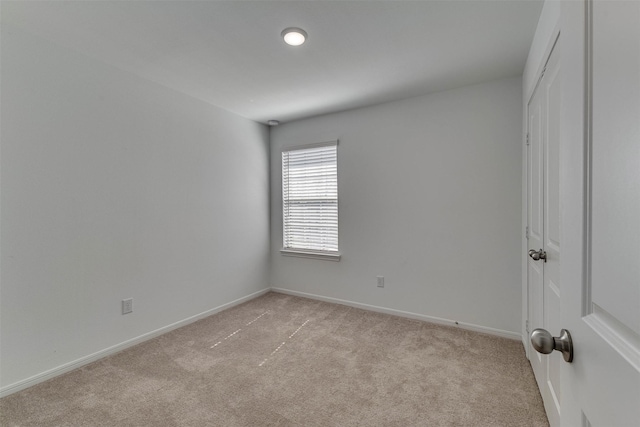 spare room featuring light colored carpet and baseboards