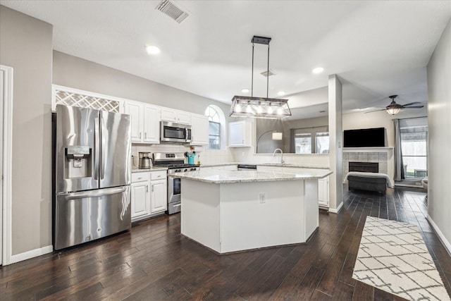 kitchen featuring white cabinets, light stone counters, hanging light fixtures, stainless steel appliances, and a sink