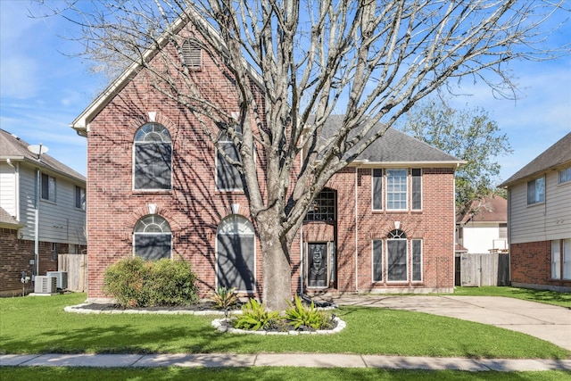 view of front facade with brick siding, a shingled roof, fence, driveway, and a front lawn