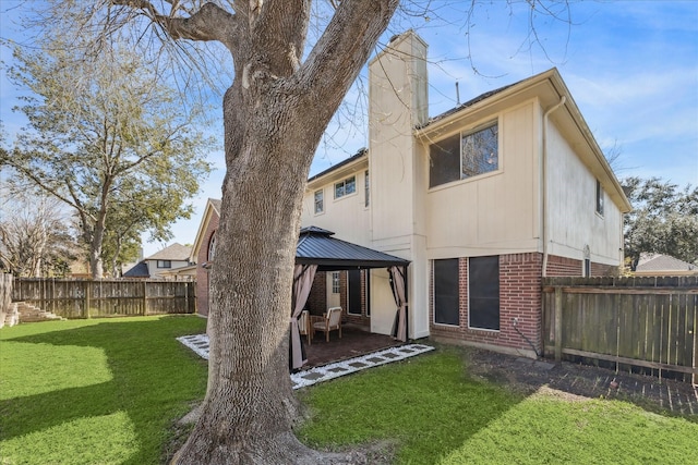 rear view of house featuring a fenced backyard, brick siding, a gazebo, a lawn, and a chimney