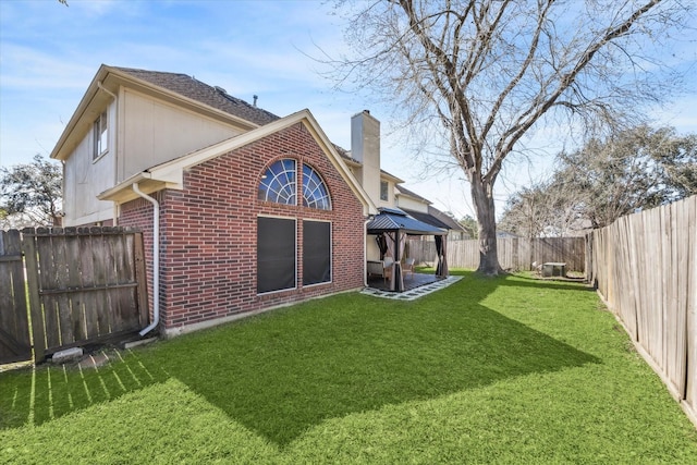 back of property with brick siding, a chimney, a lawn, a gazebo, and a fenced backyard