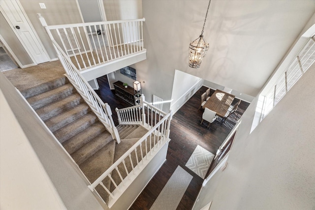 stairway with a chandelier, wood finished floors, a towering ceiling, and baseboards