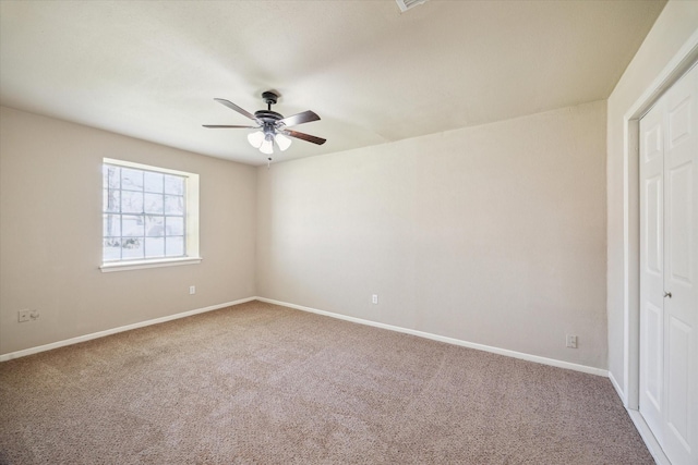 carpeted spare room featuring ceiling fan and baseboards