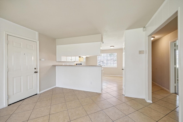 kitchen with light tile patterned flooring, a peninsula, light countertops, and baseboards