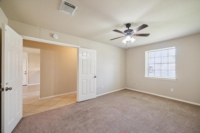 carpeted empty room with visible vents, baseboards, ceiling fan, and tile patterned flooring