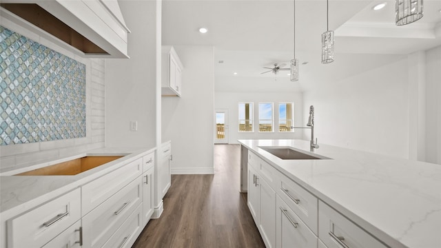 kitchen featuring a ceiling fan, light stone counters, hanging light fixtures, white cabinetry, and a sink