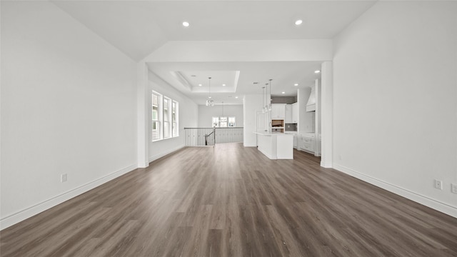 unfurnished living room featuring a notable chandelier, baseboards, a raised ceiling, and dark wood-style flooring