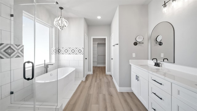 bathroom featuring wood finished floors, vanity, a spacious closet, a soaking tub, and a stall shower