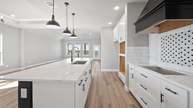 kitchen with pendant lighting, a kitchen island with sink, white cabinets, a sink, and premium range hood