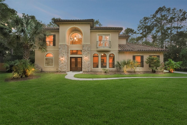 mediterranean / spanish-style home featuring a balcony, a tile roof, a yard, french doors, and stucco siding