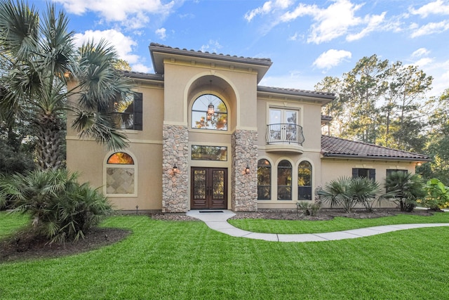 view of front facade with a balcony, stucco siding, a front lawn, and french doors