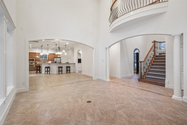 living area with arched walkways, decorative columns, a towering ceiling, and stairs