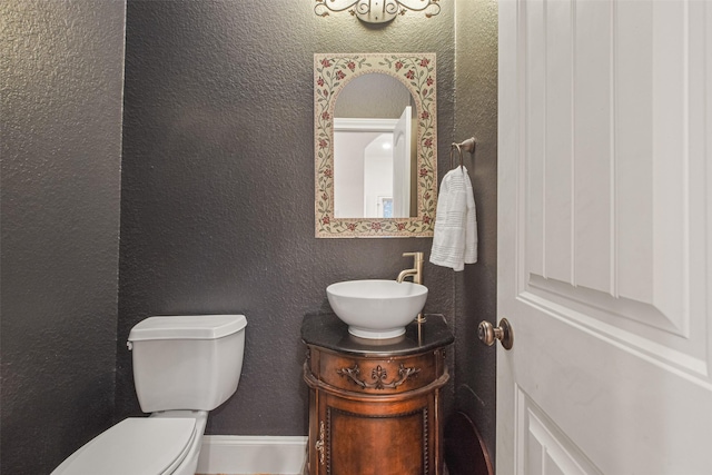 half bathroom featuring a textured wall, vanity, and toilet