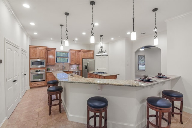 kitchen with arched walkways, stainless steel appliances, a peninsula, a center island, and a kitchen bar