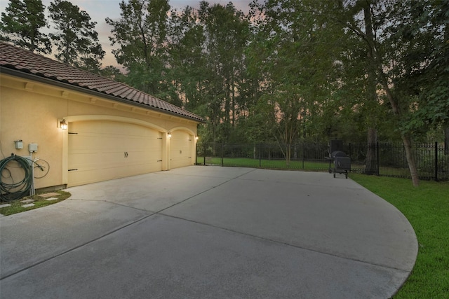 garage at dusk with fence, a lawn, and concrete driveway