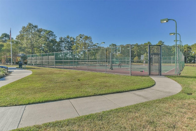 view of community with a yard, a tennis court, and fence