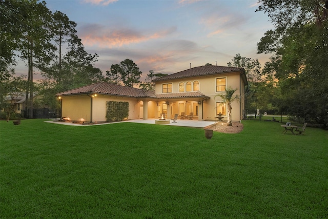 back of property at dusk with a patio area, a tile roof, stucco siding, and a yard