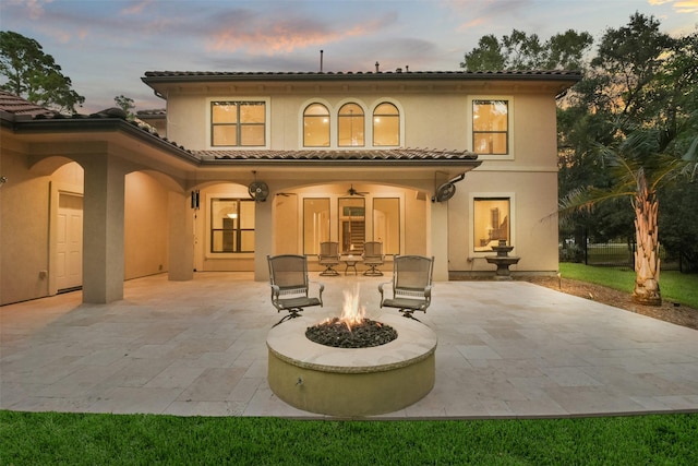 rear view of house featuring stucco siding, a tile roof, a fire pit, and a patio