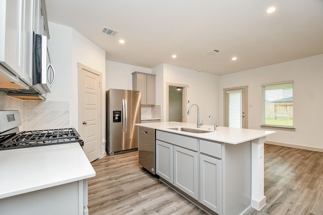 kitchen featuring stainless steel appliances, a sink, visible vents, light countertops, and an island with sink