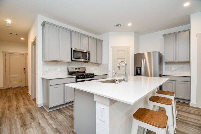 kitchen with stainless steel appliances, a sink, light countertops, a kitchen bar, and a center island with sink