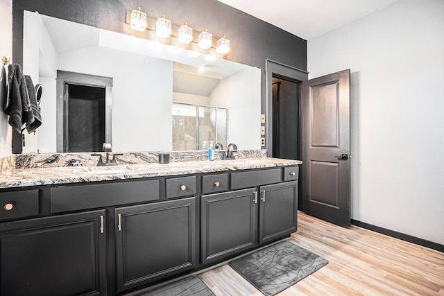 full bath with a stall shower, double vanity, a sink, and wood finished floors