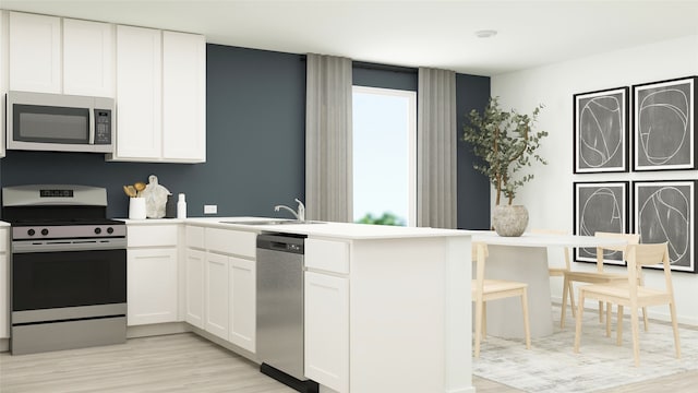 kitchen featuring a sink, white cabinetry, a peninsula, stainless steel appliances, and light wood-type flooring