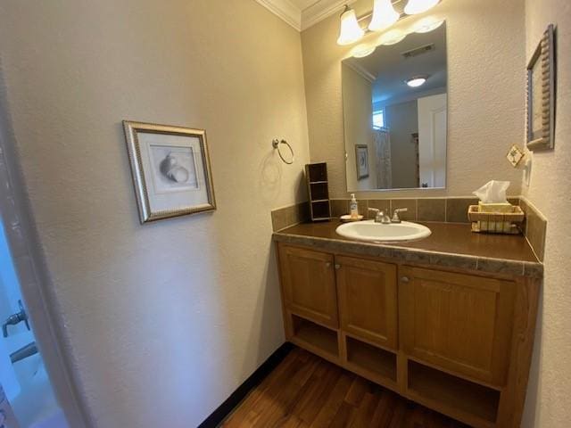 bathroom featuring baseboards, visible vents, ornamental molding, wood finished floors, and vanity