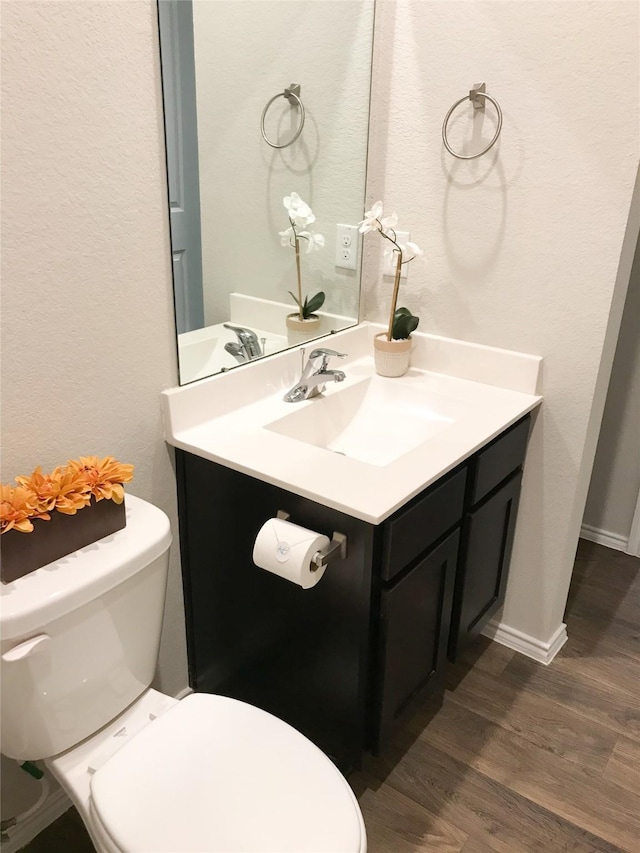 half bathroom with baseboards, vanity, toilet, and wood finished floors